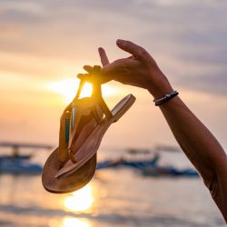 Woman on the beach in Bali Indonesia holding her sandals sunset SANDALS